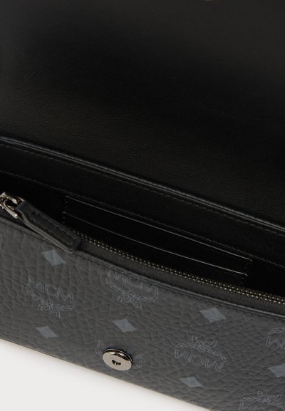 Μαύρη δερμάτινη γυναικεία τσάντα με υφή γκρι κάτω μέρος που διαθέτει μοτίβο λογότυπου MCM. Το άνοιγμα με φερμουάρ αποκαλύπτει εσωτερικές θήκες για κάρτες και λείο επένδυση.