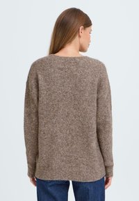 Brown, soft, knitted sweater with a round neck, dropped shoulders, and ribbed cuffs. The fabric has a fuzzy texture and a loose fit.