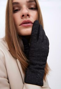 Černé prošívané rukavice s texturovaným vzorem a embosovaným nápisem. Vyrobené z měkké tkaniny, navržené s elegantním střihem a akcentem loga.