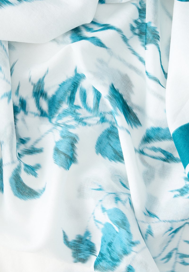 White fabric with soft teal floral and leaf patterns, showing gentle folds and a smooth texture.