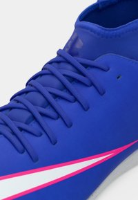 Φωτεινό μπλε αθλητικό παπούτσι με λεία, συνθετική επάνω επιφάνεια, με μωβ κορδόνια και μια τολμηρή ροζ και λευκή ρίγα στην πλευρά.