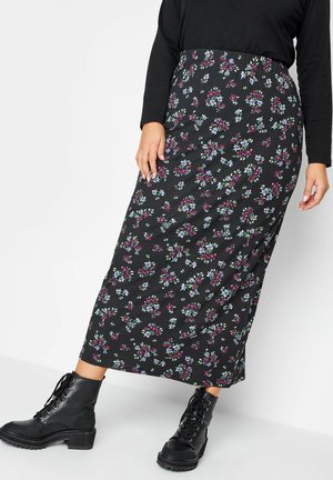 Woman wearing a black floral midi skirt with purple and blue flowers, paired with black lace-up ankle boots and a black long-sleeve top.