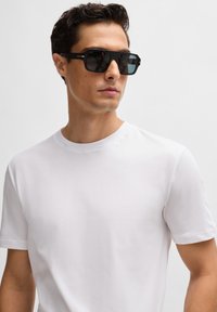 Black rectangular sunglasses with a matte finish and slight blue tint, worn with a plain white crewneck t-shirt. Smooth texture overall.