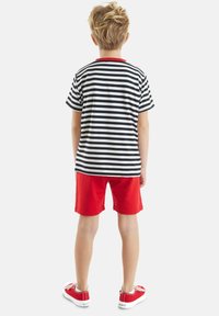 Sort-hvid stribet t-shirt med rød krave, parret med røde shorts. Barnets rygvisning, iført røde sneakers med hvide detaljer.