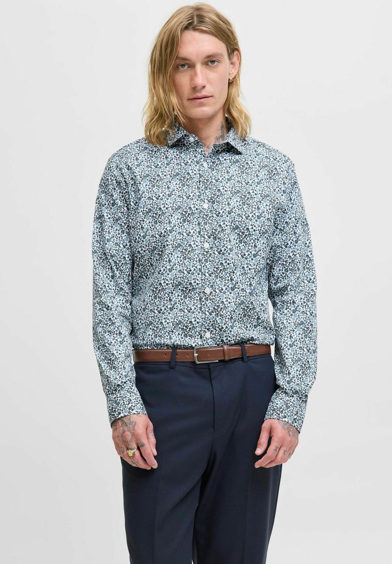 Camicia button-up con stampa floreale blu, maniche lunghe, in cotone, colletto, abbinata a pantaloni blu navy e una cintura in pelle marrone.