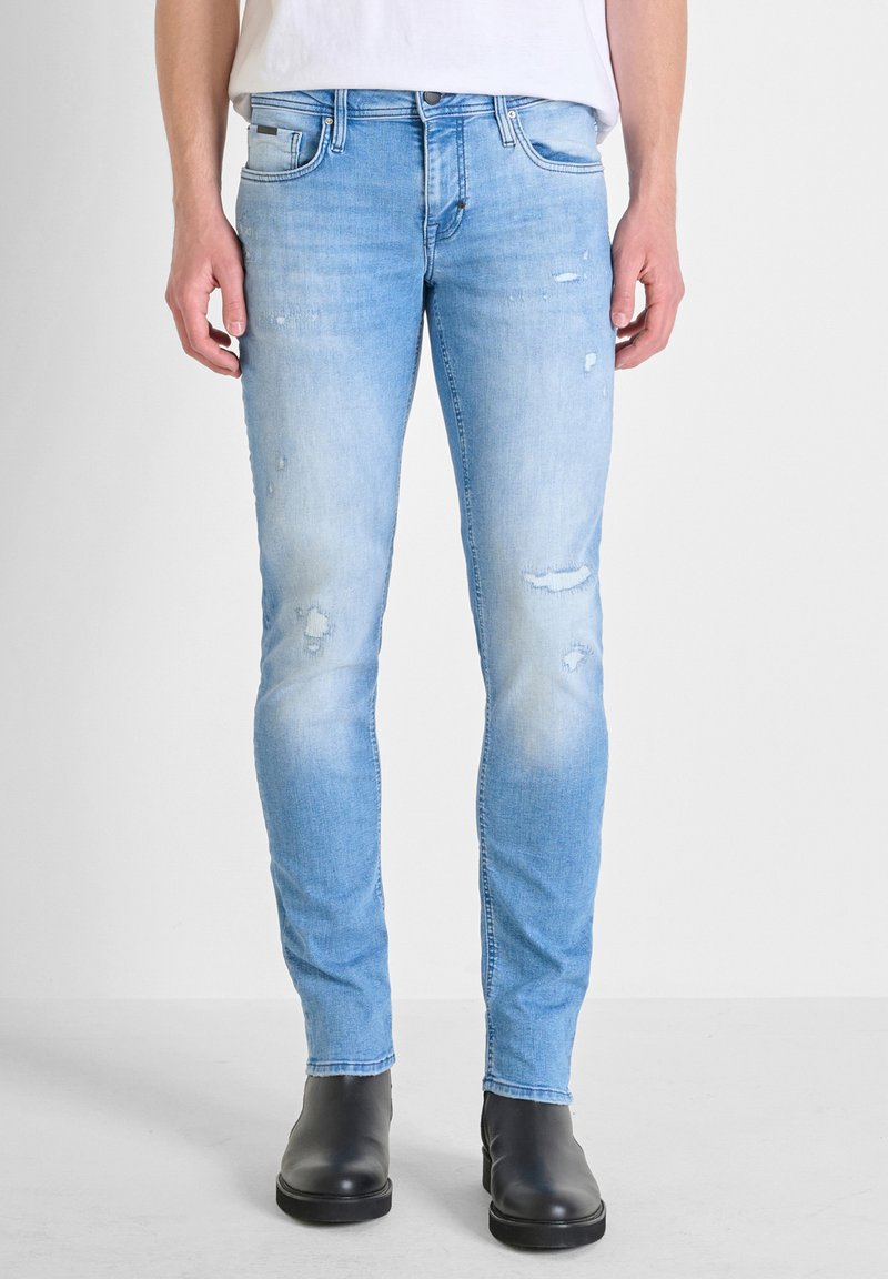 Jeans azzurri chiaro con una vestibilità slim, dettagli strappati e effetti di scoloritura sulle cosce. Abbinati a stivali neri alla caviglia.