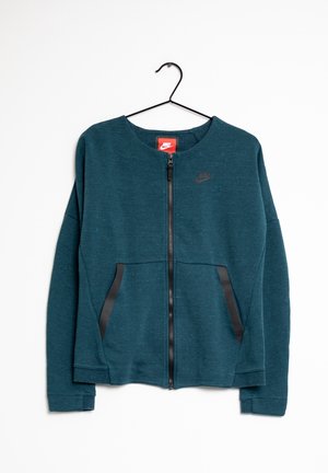 Donkerteal Nike-jas met ritssluiting, zakken met zwarte biezen, lange mouwen en een ronde hals, hangend aan een zwarte hanger.
