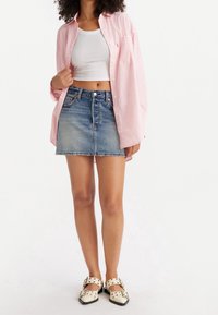 Lichtroze gestreept overhemd met knopen, wit cropped tanktop, blauwe denim minirok en crèmekleurige schoenen met zwarte accenten en banddetail.