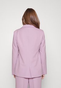 Fialový blazer s přiléhavým střihem, klopovými límci a rozparkem na zadní straně. Hladká tkanina s čistým povrchem, doplněná o odpovídající kalhoty.