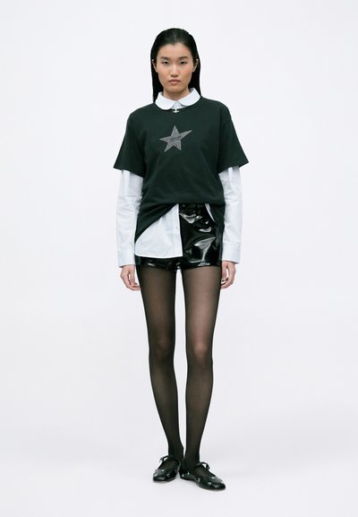 Tricou negru cu grafică de stea argintie peste o cămașă albă cu guler, asociat cu pantaloni scurți negri lucioși și colanți negri translucizi, completat cu încălțăminte neagră.
