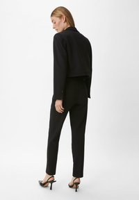 Zwarte cropped blazer met een gepast model, lange mouwen en met een notch-lapel, gecombineerd met zwarte slim-fit broeken en haksandalen.