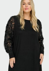 Sort kjole med lange, gjennomsiktige puffermede ermer med rysjedetaljer; laget av mykt materiale; avslappet passform, rund hals.