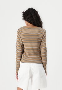 Langermet brunstripet topp med hvite og mørkere striper, med rund hals og ribbet tekstur, kombinert med hvite shorts.