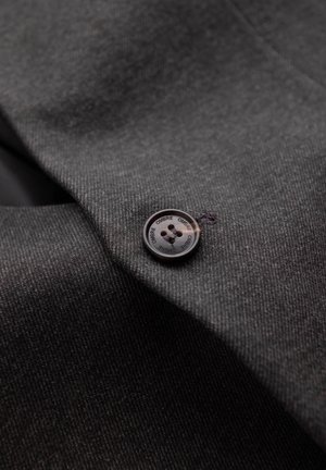 Tejido gris que muestra un primer plano de un botón, con un diseño redondo, una superficie lisa y cuatro orificios, cosido con hilo oscuro.