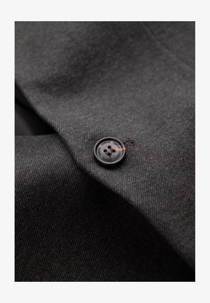Grauer Stoff zeigt eine Nahaufnahme eines Knopfes mit rundem Design, glatter Oberfläche und vier Löchern, genäht mit dunklem Faden.