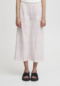 Pantalons larges blancs avec un motif vertical rose et vert, dotés d'une ceinture confortable et de poches latérales. Portés avec des sandales noires.