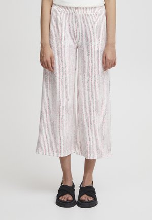 Pantalons larges blancs avec un motif vertical rose et vert, dotés d'une ceinture confortable et de poches latérales. Portés avec des sandales noires.