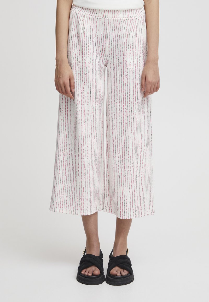 Pantalons larges blancs avec un motif vertical rose et vert, dotés d'une ceinture confortable et de poches latérales. Portés avec des sandales noires.