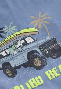 Lyseblå T-shirt med et grafisk tryk af et blåt terræn køretøj med gule detaljer, der bærer et grønt surfbræt, omgivet af palmer.