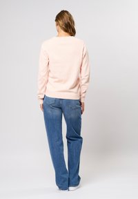 Světlý růžový svetr s kulatým výstřihem, žebrovanými manžetami a lemem. Kombinován se širokými modrými džínami s kapsami na zadní straně a lehkým opráním.