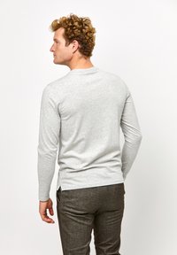 Helle graue Langarmshirt mit rundem Hals, glatter Textur und seitlichen Schlitzen, kombiniert mit dunkel strukturierten Hosen.