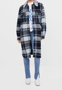Károvaný vlněný kabát v námořnické modré, černé a bílé barvě s modrým akcentem. Zapínání na knoflíky, límec, dvě náprsní kapsy a dlouhé rukávy.