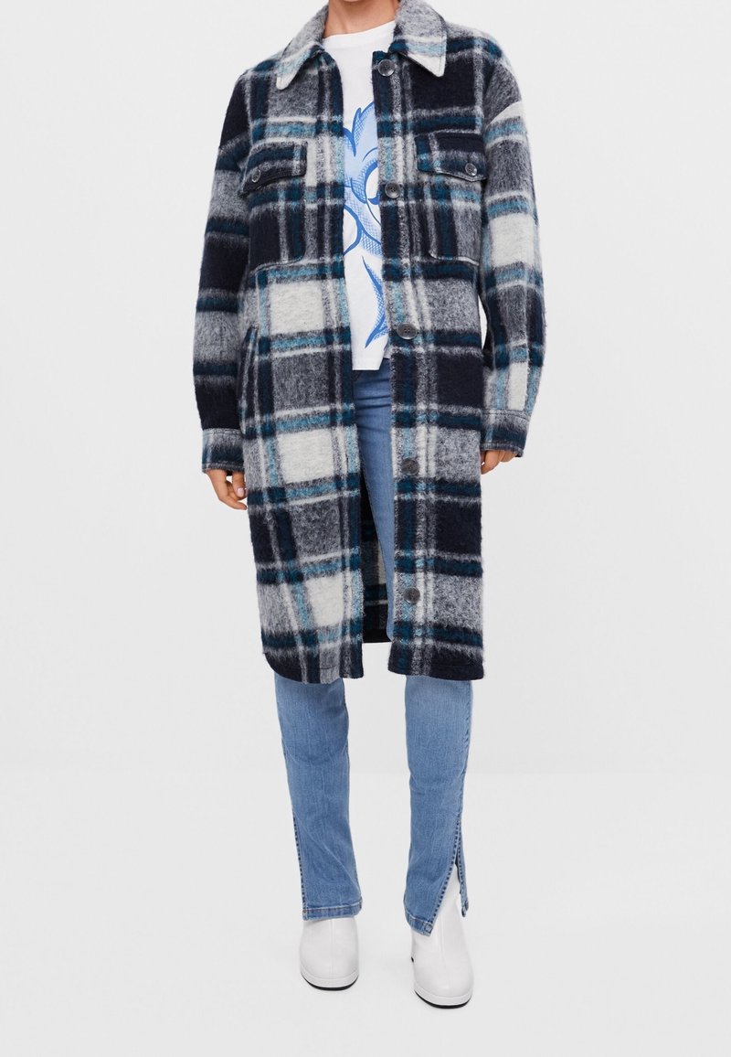 Károvaný vlněný kabát v námořnické modré, černé a bílé barvě s modrým akcentem. Zapínání na knoflíky, límec, dvě náprsní kapsy a dlouhé rukávy.