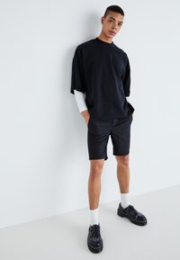Svart oversized t-shirt med korta ärmar i kombination med svarta shorts. Outfiten har en avslappnad passform och kompletteras med svarta skor och vita strumpor.