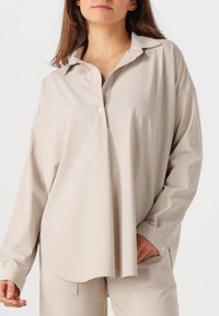 Beige Button-up-Hemd mit kragenförmigem Ausschnitt, langen Ärmeln, lockerer Passform und glatter Stoffstruktur, mit einem abgerundeten Saum.