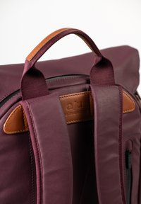 Zaino bordeaux con una superficie in tessuto liscio, dettagli in pelle marrone, spallacci imbottiti e una maniglia superiore. Presenta un compartimento con zip.