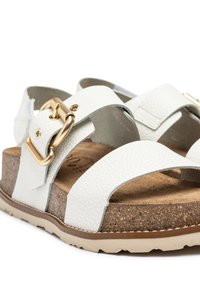 Sandalias de cuero blanco con dos correas anchas, un acento de hebilla dorada, una plantilla de corcho y suela de goma texturizada.