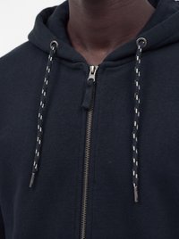 Gros plan d'une personne portant un sweat à capuche zippé foncé avec des cordons à motifs et une fermeture éclair en métal visible au niveau du cou.