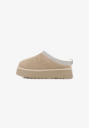 Zapato de ante beige tipo slip-on con un borde tejido en azul claro texturizado, suela de plataforma elevada y diseño de punta redonda.