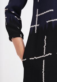  mustapuku, jossa on kuviointi, jossa on vaaleanharmaita risteyttäviä viivoja, pitkät hihat ja hieman rento istuvuus.