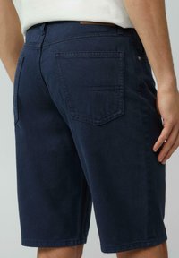Granatowe dżinsowe szorty o luźnym kroju, z dwiema tylnymi kieszeniami i gładką fakturą. Skórzany akcent przy pasku.