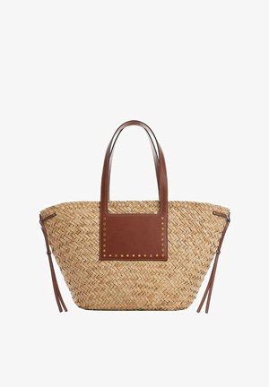 Sac fourre-tout en paille tissée avec poignées en cuir marron, patch rectangulaire en cuir et accents de pampilles en cuir sur les côtés.