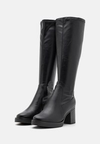 Bottes noires à hauteur de genou en cuir lisse avec un talon carré, présentant un design élégant et des coutures minimales le long des bords.