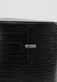 Mustan korkeasti kohokuvioidun nahkalaukun, jossa on tekstuuri krokotiilimuotoilulla, varustettu tyylikkäällä hopeisella hardware-hihnakiinnityksellä.