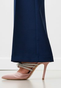 Zapato de tacón alto de satén rosa con punta afilada y tira de tobillo de cuentas plateadas, combinado con pantalones de tobillo de color marino.