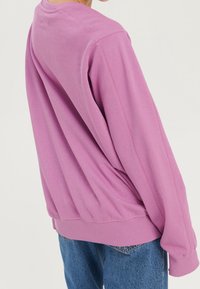 Sudadera rosa de corte relajado, con puños y dobladillo de canalé, que presenta detalles de costura. Combinada con jeans de color azul claro.
