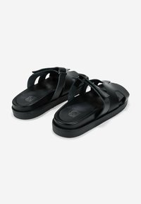 Sandalias negras con correas cruzadas anchas, plantilla contorneada y suela texturizada. Hechas de material sintético suave. Diseño de plataforma baja.