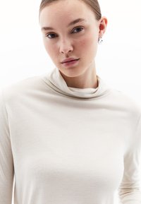 Lange mouwen turtleneck van lichtbeige stof met een soepele textuur, voorzien van een subtiele gedrapeerde kraag. Duidelijke, gelijkmatige kleur overal.
