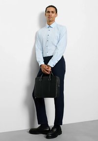 Hellblau gestreiftes Hemd mit Knöpfen und langen Ärmeln, marineblaue Hose und schwarze Lederaktentasche. Schwarze Schuhe vervollständigen das Outfit.