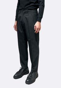 Pantaloni neri plissettati in tessuto liscio, con vestibilità classica e fronte piatto, abbinati a scarpe nere con lacci.