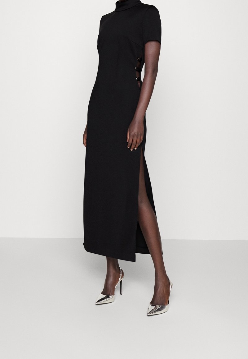 Mustapuku, jossa on lyhyet hihat, korkea kaula-aukko, sivuhalkio ja nappi-yksityiskohtia. Yhdistetty metallin värisiin korkokenkiin.