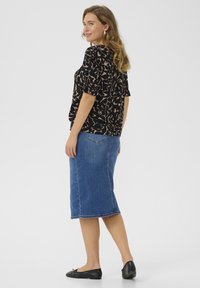 Blouse noire avec un motif abstrait beige, manches courtes bouffantes ; jupe midi en denim bleu ; ballerines noires avec un détail en nœud ; textures lisses tout au long.