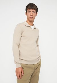 Beige gebreide poloshirt met lange mouwen en een kraag, van subtiel gestructureerde stof, gecombineerd met khaki broek.