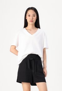 Hvit, kortermet V-hals t-skjorte kombinert med svarte, høytlivs shorts med et stoffbelte i midjen. Enkelt, rent design.
