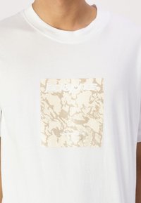Bílý bavlněný tričko s grafikou zlatého a béžového mramorového čtverce s bílým textem "jack & jones". Klasický design s kulatým výstřihem.