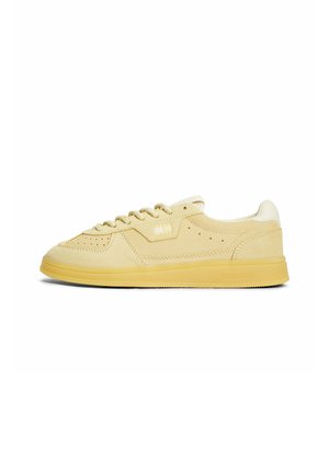 Beige lage suède sneaker met geperforeerde details, beige veters, witte gevoerde hielkraag en gele rubberen zool.